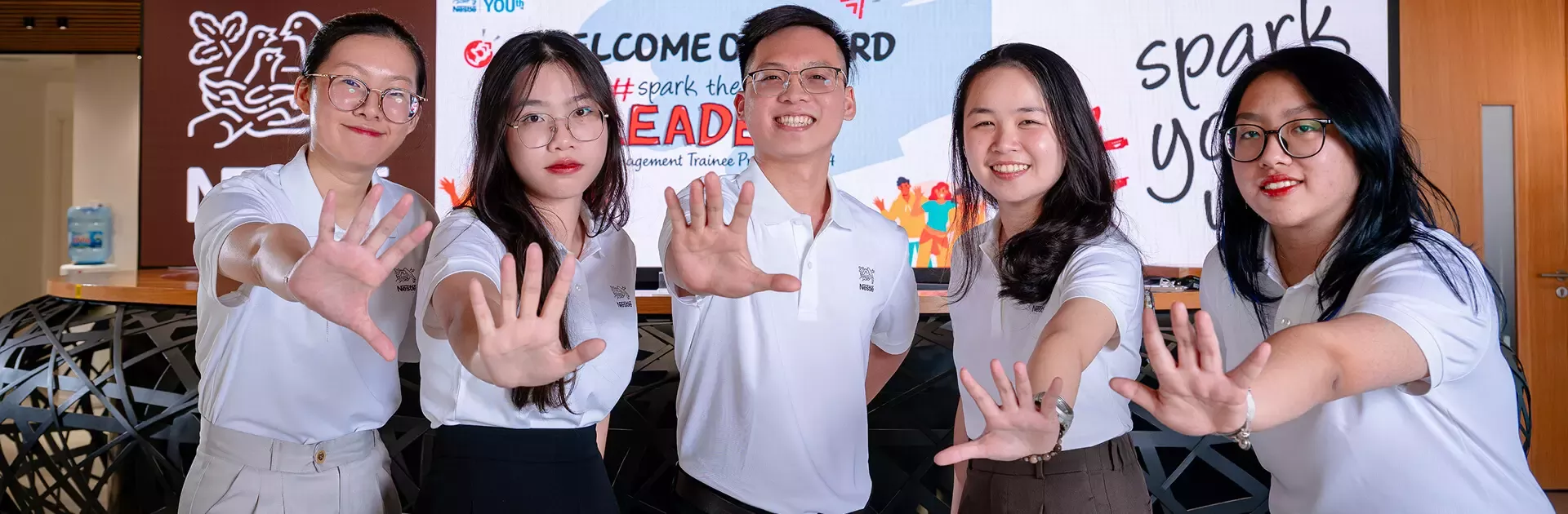 A group of young professionals in white polo shirts poses together at a Nestlé event, celebrating a management trainee progra